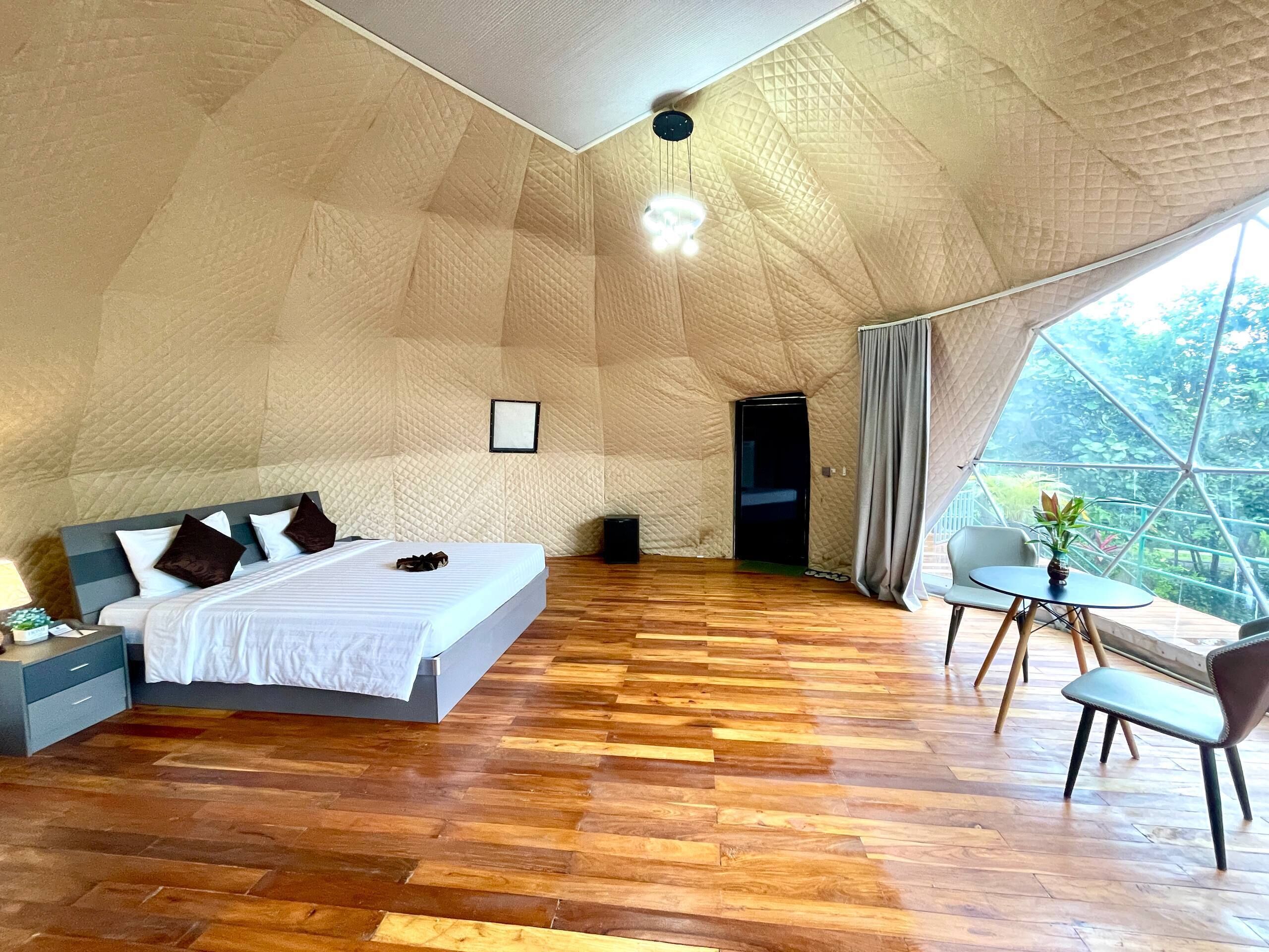 Quarto amplo com uma cama grande, uma escrivaninha e um espaço de refeições com vista através de uma janela extensa.