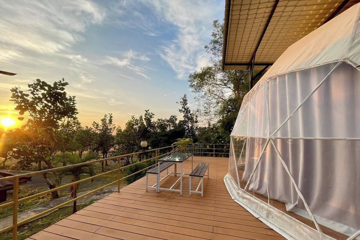 An outdoor deck with a table and chairs, a covered area, and a view of trees and the sunset.