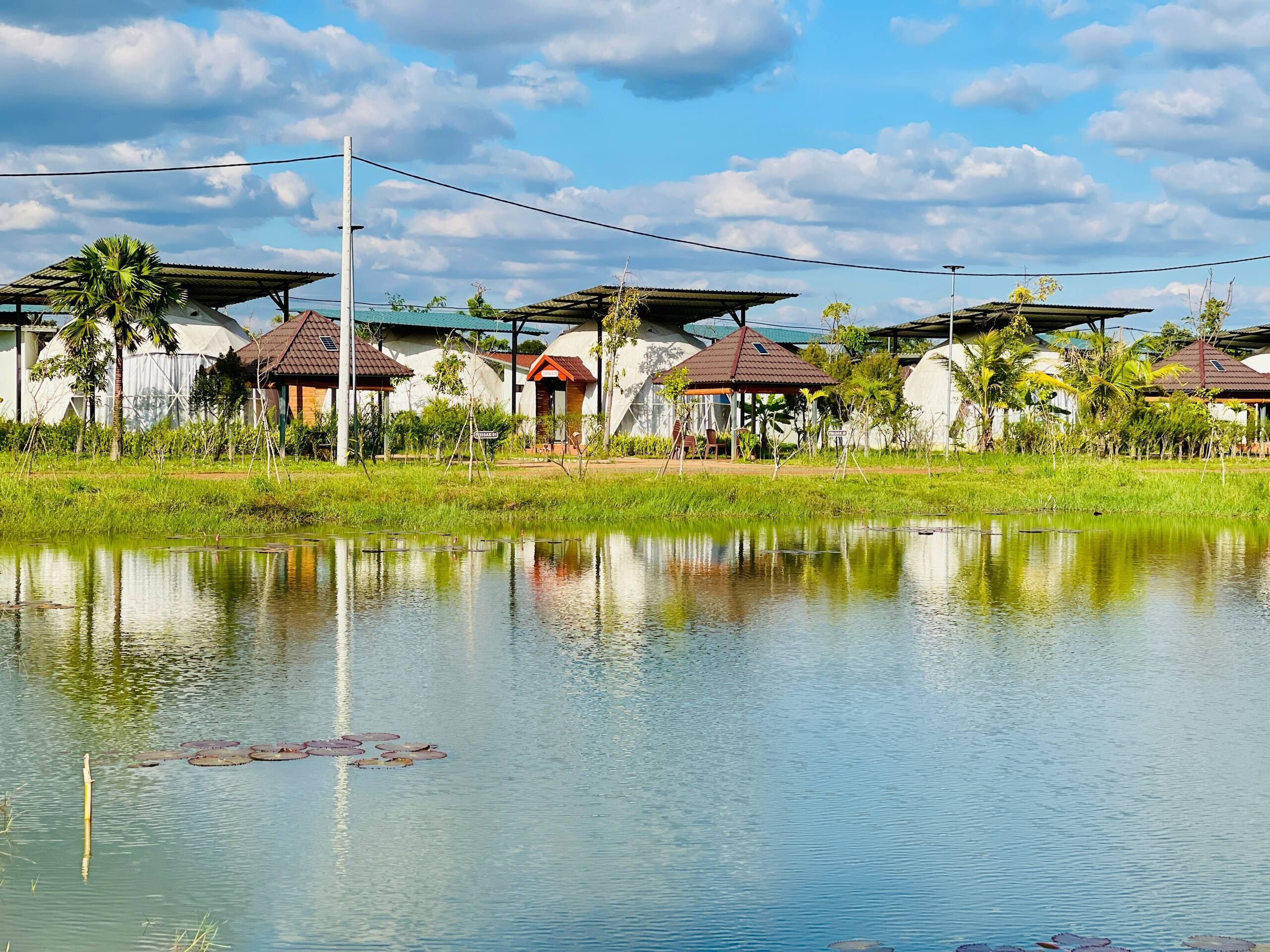 Une vue paisible sur un lac, avec une rangée de bâtiments de style traditionnel, chacun ayant un toit distinctif et étant entouré d’une végétation luxuriante.