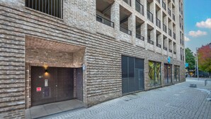 Un edifici amb façana de maó, entrada tancada i un dispositiu d'alarma contra incendis, i un carrer pavimentat al davant.