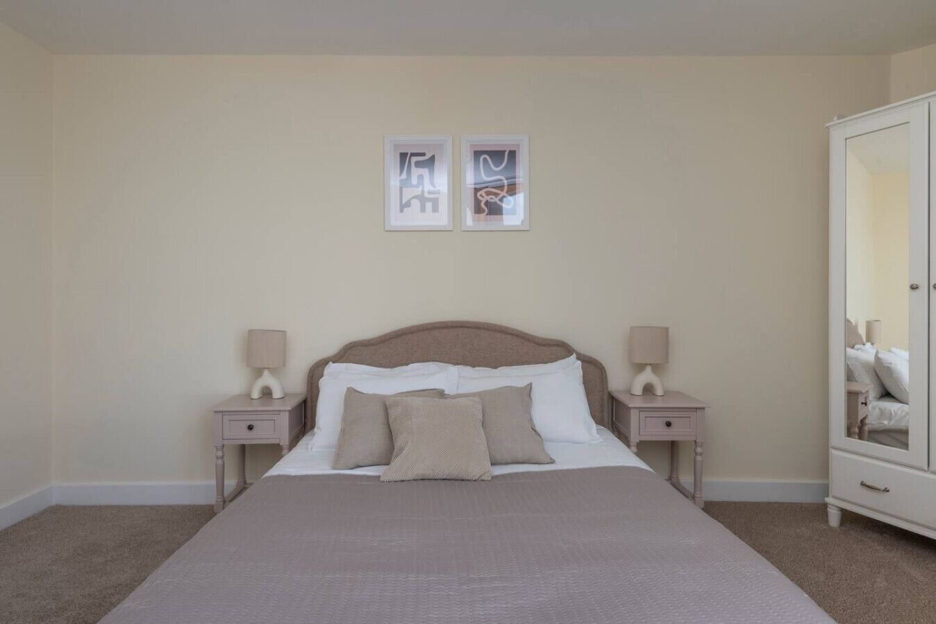 Ein Schlafzimmer mit einem großen Bett, zwei Nachttischen, einem Kleiderschrank und zwei Bilderrahmen an der Wand.