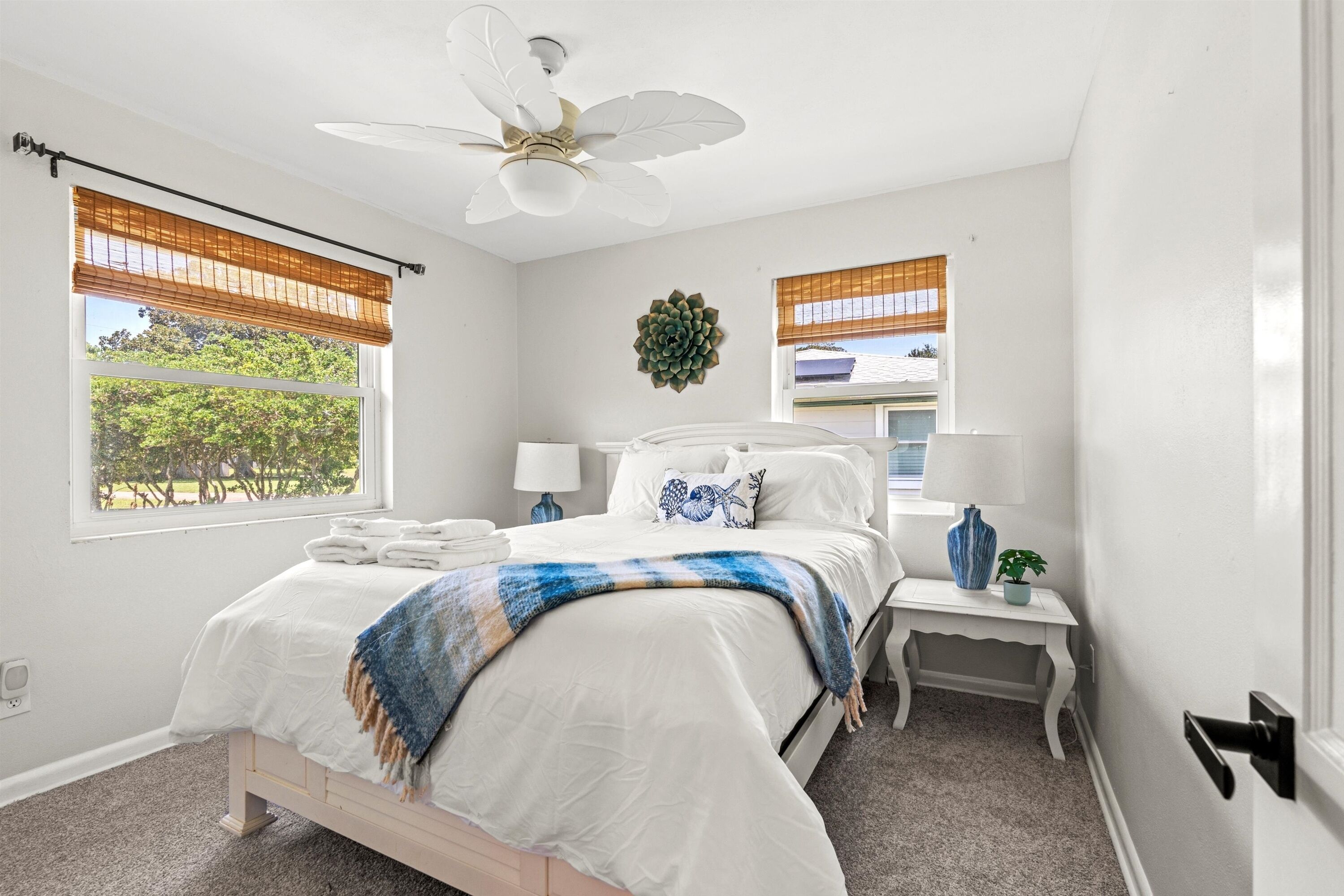 A bedroom with a bed, two bedside tables, a ceiling fan, and a window with a view of trees.