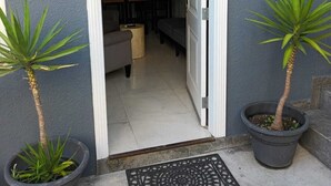 En dörröppning leder in till ett modernt kök med en matplats. På var sin sida om ingången står det två krukväxter.
