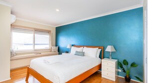 A bedroom with a bed, bedside tables, a window seat, and a potted plant. - Scarborough Seaview on Brighton (Scarborough)