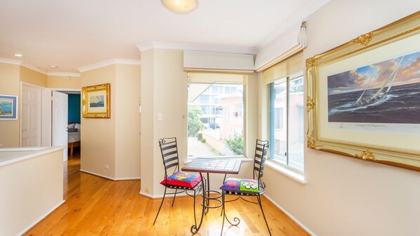 Un pasillo con piso de madera, un comedor con mesa y sillas, y un cuadro grande enmarcado en la pared.