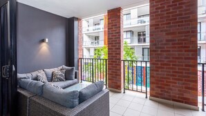 A balcony with a grey sofa, black and white patterned cushions, and a wicker chair. - Subiaco Rooftop on Sheen (Subiaco)
