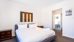 A hotel room with a large bed, a nightstand, a dresser, and a painting on the wall. - Scarborough Villa on Mickey (Scarborough)