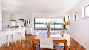 A modern kitchen with white cabinetry, a central island, and a dining area with a wooden table and white chairs. - Scarborough Villa on Mickey (Scarborough)