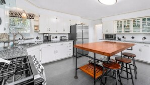 Eine moderne Küche mit weißen Schränken, einer zentralen Kochinsel mit Barhocker, Edelstahlgeräten und einer gemusterten Spritzschutzwand.