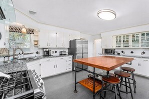 A modern kitchen with white cabinets, a central island with stools, stainless steel appliances, and a patterned backsplash. - Game Room | Fenced Yard | Fire Pit | Sleeps 8 (Galveston)