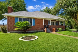 A single-story brick house with a front porch, a small front yard, and a tree.