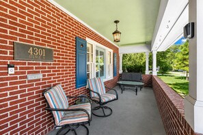 A covered porch with a brick wall, a mailbox, a street sign, and outdoor furniture. - Game Room | Fenced Yard | Fire Pit | Sleeps 8 (Galveston)
