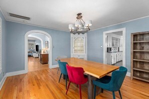 Un comedor con una mesa y sillas de madera, una araña y una cocina al fondo.