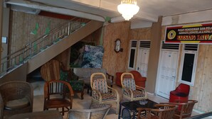 A hotel lobby with a staircase, wicker furniture, a chandelier, and a sign indicating amenities.