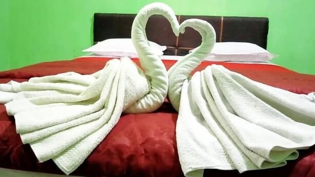 A bed with a red bedspread and white towels arranged in the shape of swans.