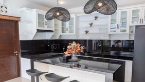 A modern kitchen with white cabinets, black countertops, and three black bar stools.