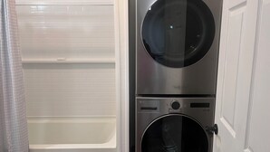 Eine kompakte Wasch- und Trocknerkombination in einem Badezimmer mit weiß gefliesten Wänden und einer Duschvorhang.
