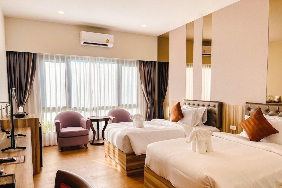 A hotel room with two beds, a desk, a chair, and a large window with curtains.