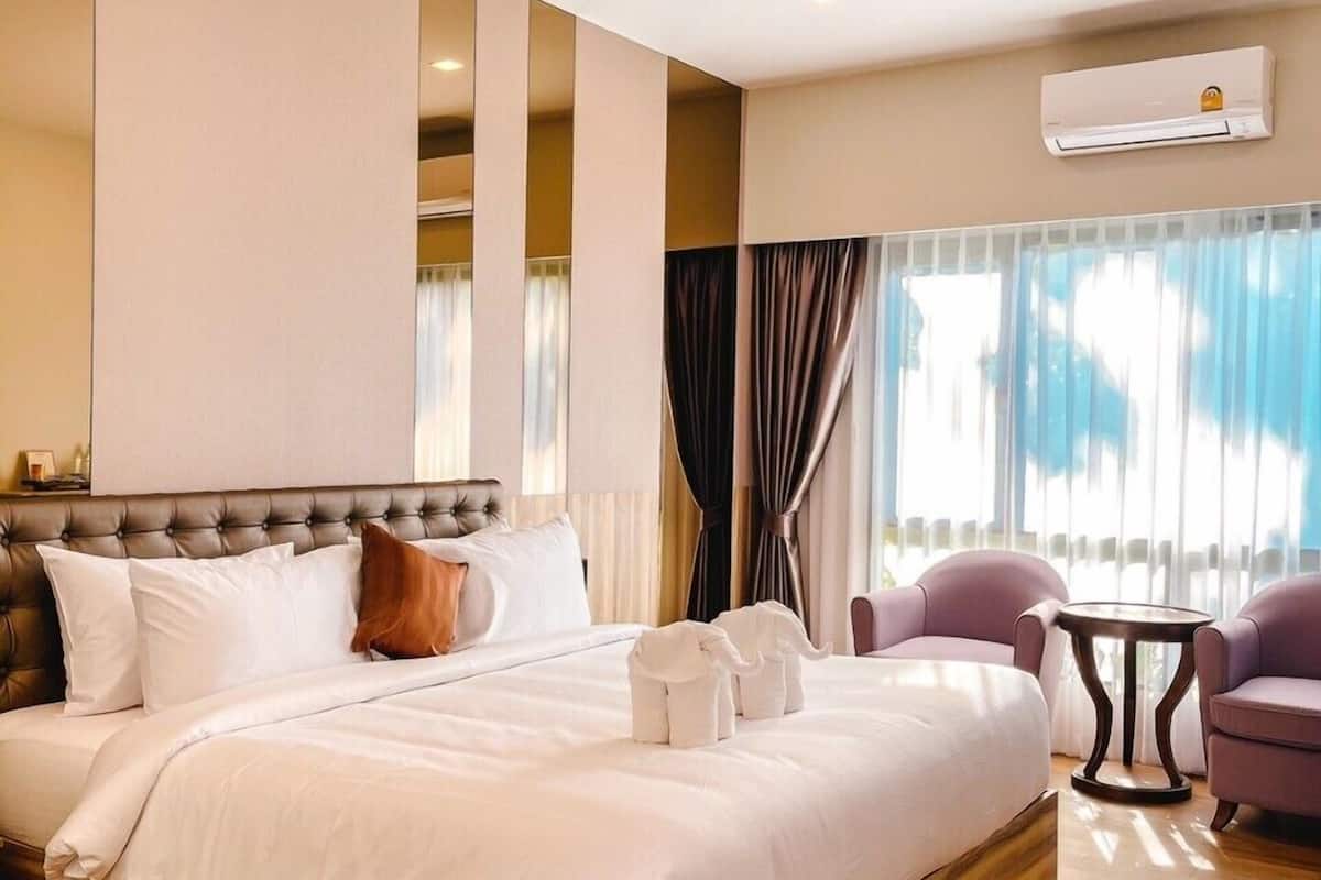 A hotel room with a large bed, a small round table, and two armchairs.