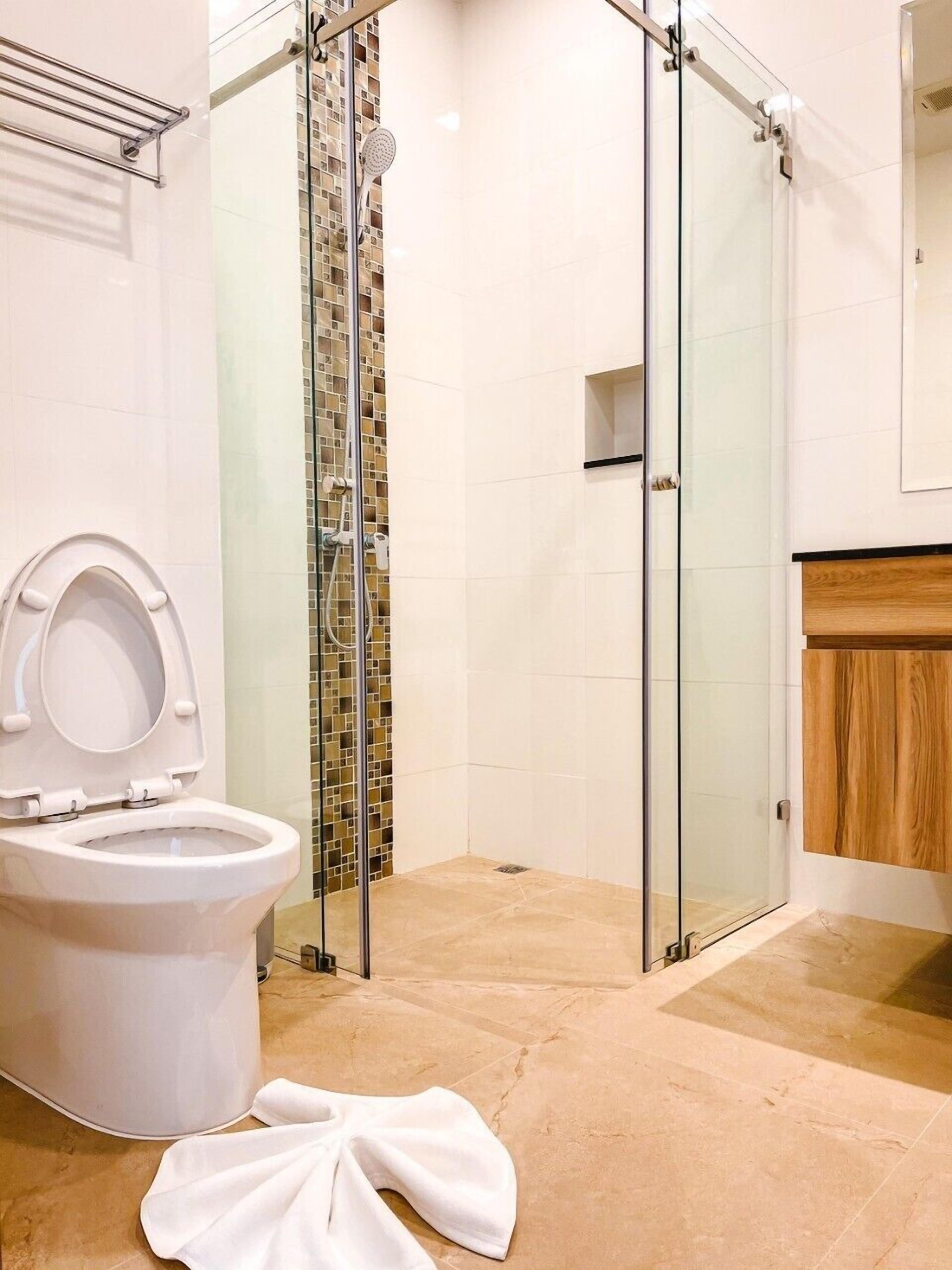 A modern bathroom with a glass-enclosed shower, a white toilet, and a wooden vanity.