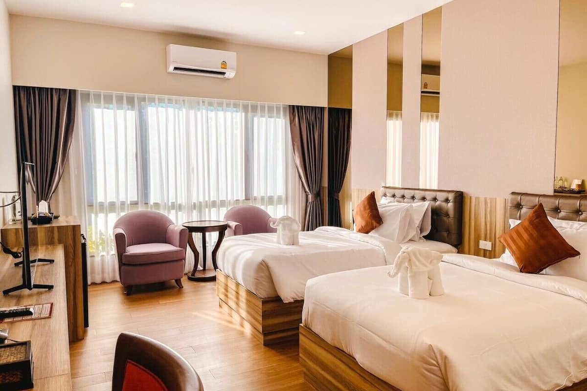 A hotel room with two beds, a desk, a chair, and a window with curtains.