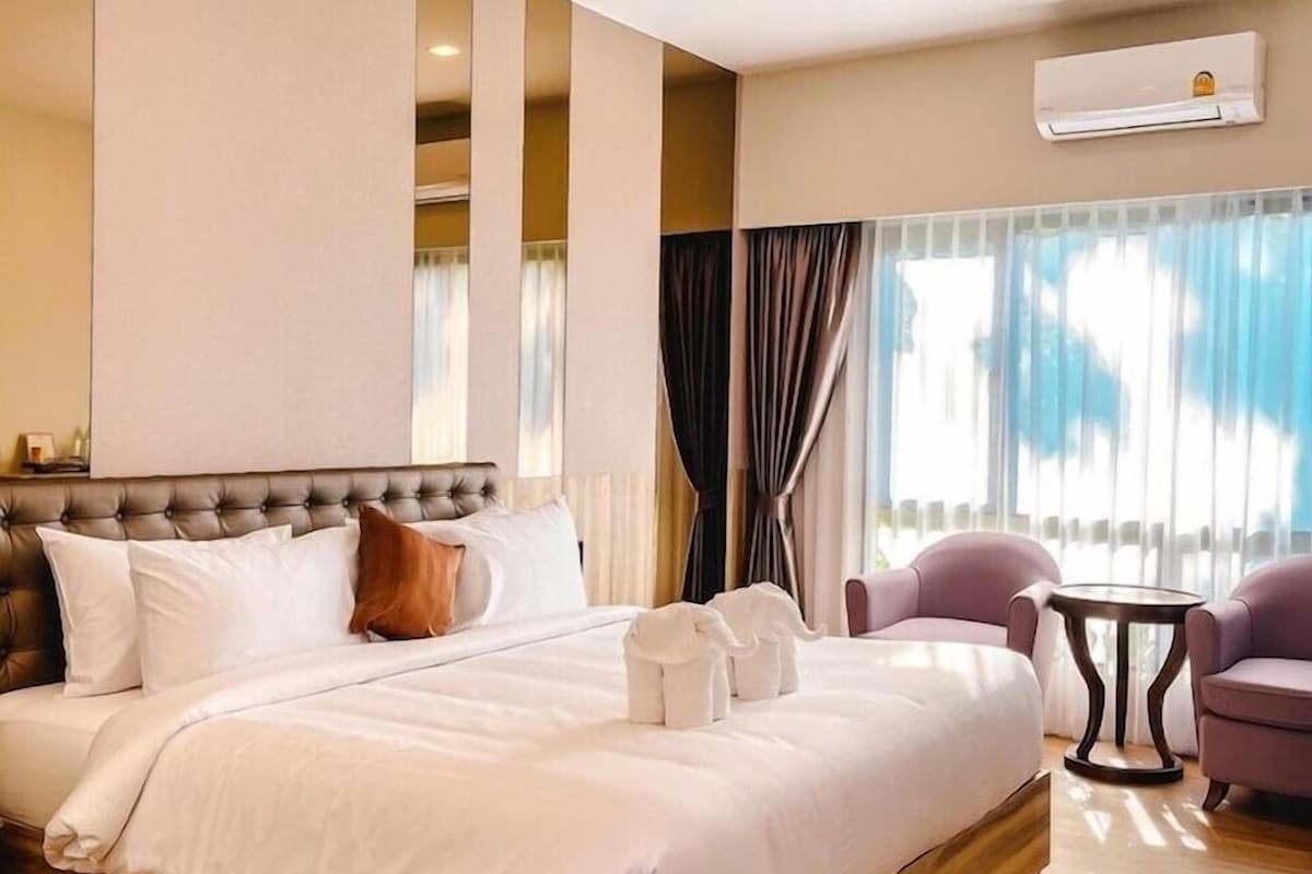 A hotel room with a large bed, a small table, two chairs, and an air conditioning unit.