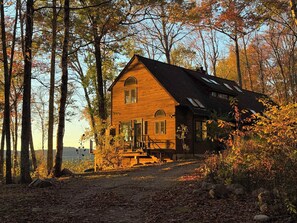 A rustic cabin with a steeply pitched roof, a front porch, and a visible staircase leading to the entrance. - Hilltop Escape with Views & Hot Tub (New Marlborough)