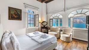 A bedroom with a bed, two chairs, a mirror, and a painting.