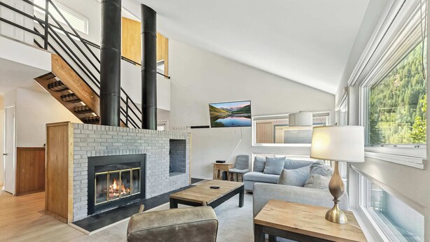 A spacious living area with a fireplace, a sofa, a coffee table, and a lamp. A staircase with a railing is visible in the background.