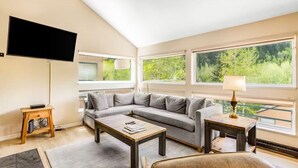 A modern living room with a grey sectional sofa, a wooden coffee table, and a TV mounted on the wall.