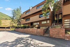 A multi-story building with a brick facade, large windows, and a staircase leading to the entrance. - East Vail Condo | Shared Pool & Hot Tub (Vail)
