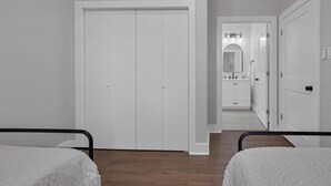Une chambre avec deux lits, une armoire blanche et une salle de bain visible à travers une porte ouverte.