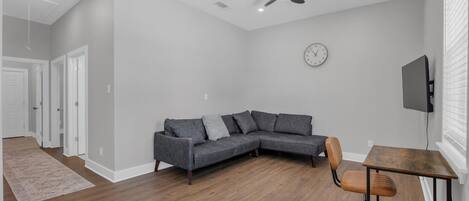 Ein modernes Wohnzimmer mit einer Eckcouch, einem Holztisch und einem Deckenventilator.