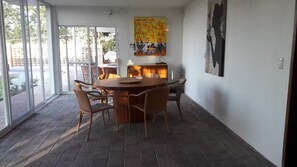 A dining area with a round table and chairs, a large window, and a painting on the wall.