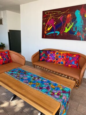 A modern living room with a sofa and bench, a colorful abstract painting, and a potted plant.