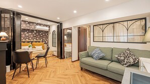 A modern living room with a green sofa, wooden herringbone flooring, a dining area with chairs, and a kitchen visible through an open door. - Designer-style 2-bedroom apartment & large living room Max 7people Shinjuku 501 (新宿区)