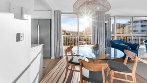 A modern kitchen with a glass dining table, wooden chairs, and a hanging light fixture.