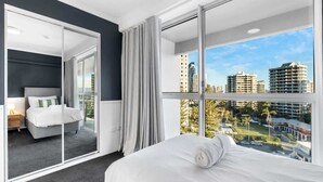 A modern hotel room with a large bed, a sliding glass door leading to a balcony, and a city view.