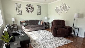 Una sala de estar con sofá, sillón y una mesa de centro. Incluye decoraciones en la pared y una lámpara de pie.