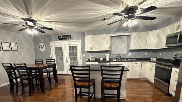 Una cocina moderna con comedor, que incluye una isla central, armarios blancos y un ventilador de techo.