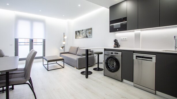 Una cocina moderna con electrodomésticos integrados, un comedor con mesa y sillas, y un sofá.