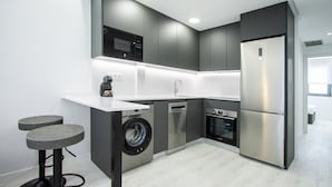 Una cocina moderna con armarios grises, un refrigerador de acero inoxidable, horno empotrado y lavadora.