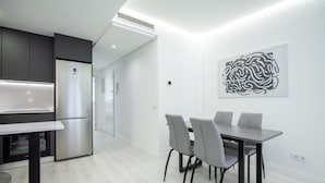 Una cocina moderna con horno empotrado y refrigerador de acero inoxidable. Hay un comedor con una mesa y cuatro sillas.