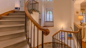 A grand staircase with a wooden handrail and metal balusters, leading to a second-floor landing with a view of the outdoors.