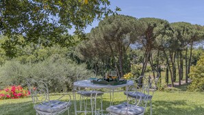 An outdoor dining area with a round table and six chairs, surrounded by lush greenery and trees.