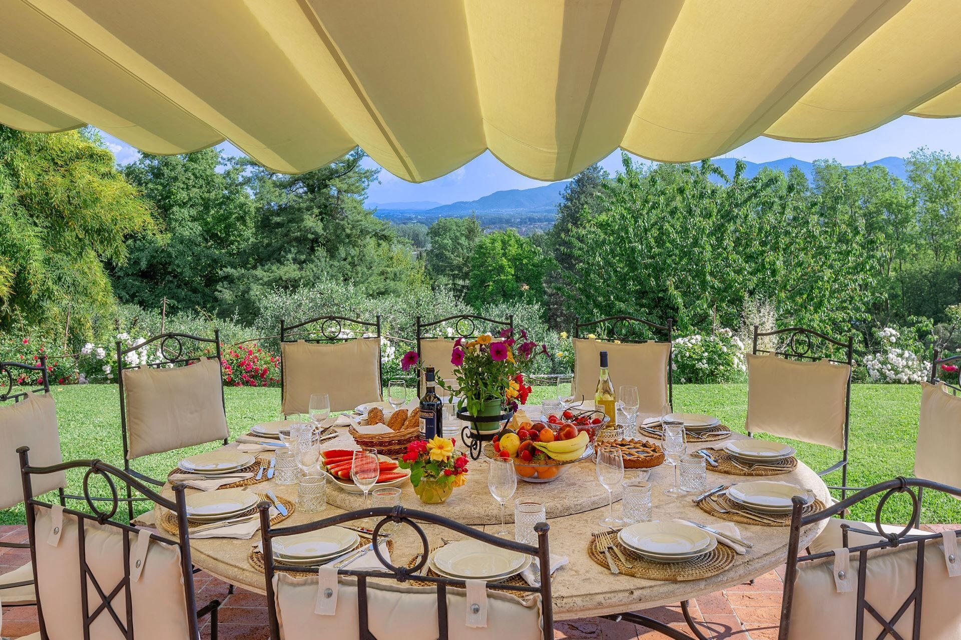 A round table set for a meal with chairs, a tablecloth, and a view of a mountainous landscape.