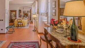 A spacious dining area with a long table set for a meal, a mirror reflecting the room, and a vase with flowers on a side table.