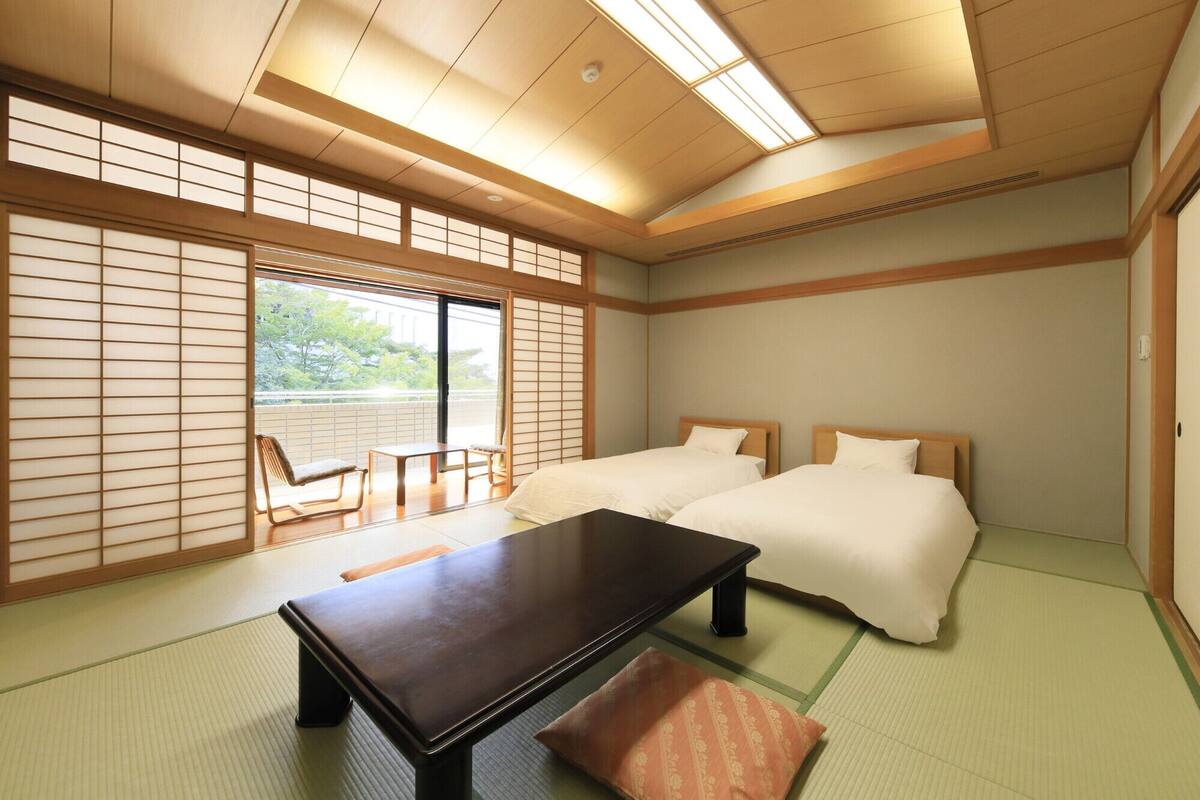 A traditional Japanese-style room with tatami flooring, a low table, two beds, and sliding shoji doors.