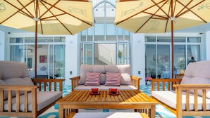 A sunlit outdoor seating area with wooden furniture, striped cushions, and umbrellas. - Mia Hot Springs Pool Villa Binh Chau (Ho Chi Minh City)