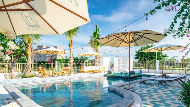 A swimming pool with lounge chairs and umbrellas, surrounded by palm trees and a patterned floor. - Mia Hot Springs Pool Villa Binh Chau (Ho Chi Minh City)
